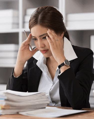 Female employee looking overwhelmed and stressed at desk with papers